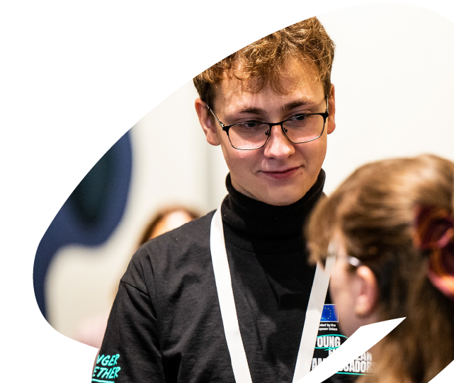 Young participant engaging in discussion during an EU4Youth youth leadership or civic engagement activity, interacting with another participant at an event.