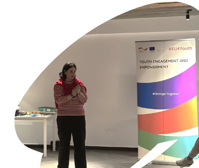 Facilitator speaking during an EU4Youth youth engagement session, standing beside an EU4Youth banner in a training or workshop setting.